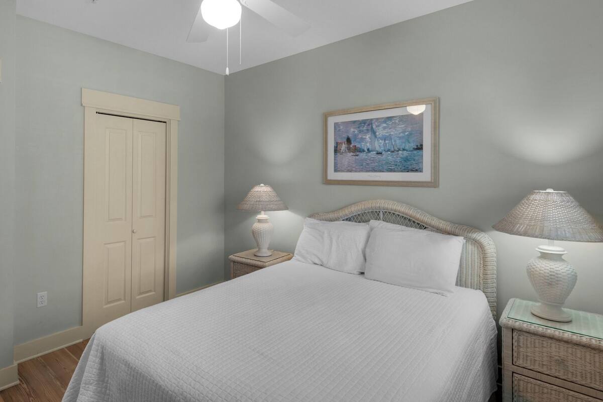 A bedroom with a bed, two bedside lamps, a painting on the wall, and a door leading to a bathroom.