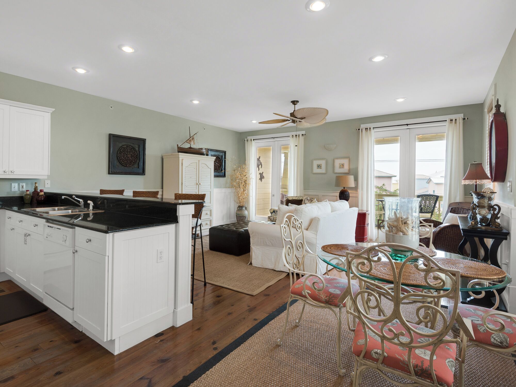 A spacious kitchen with white cabinetry, a black countertop, and a dining area with wicker chairs and a glass table.