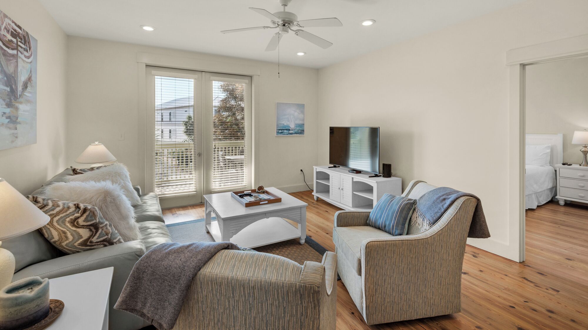 A modern living room with a sofa, armchair, coffee table, TV, and a ceiling fan.