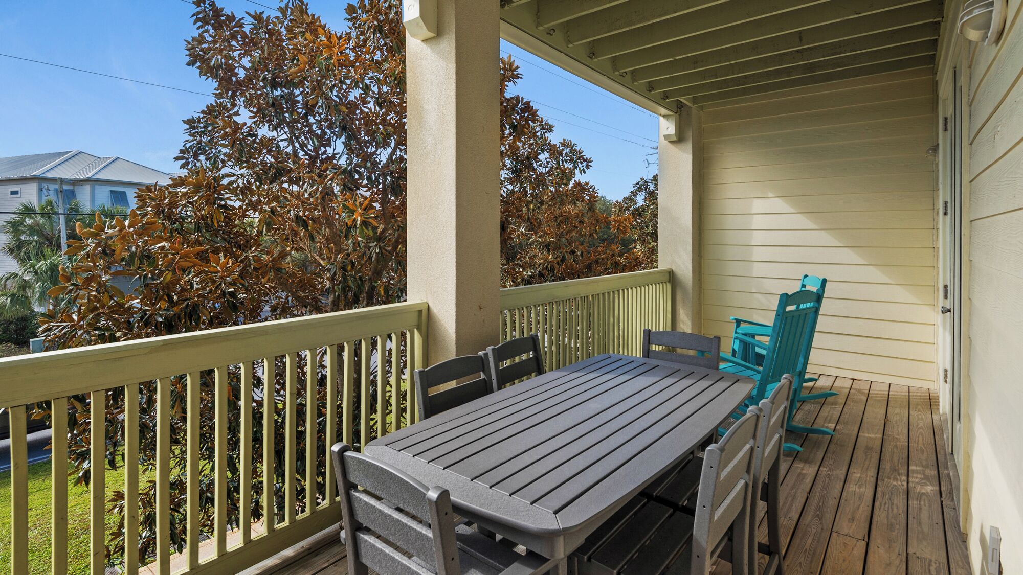 A covered outdoor patio with a table and chairs, a wooden deck, and a view of a house and trees.