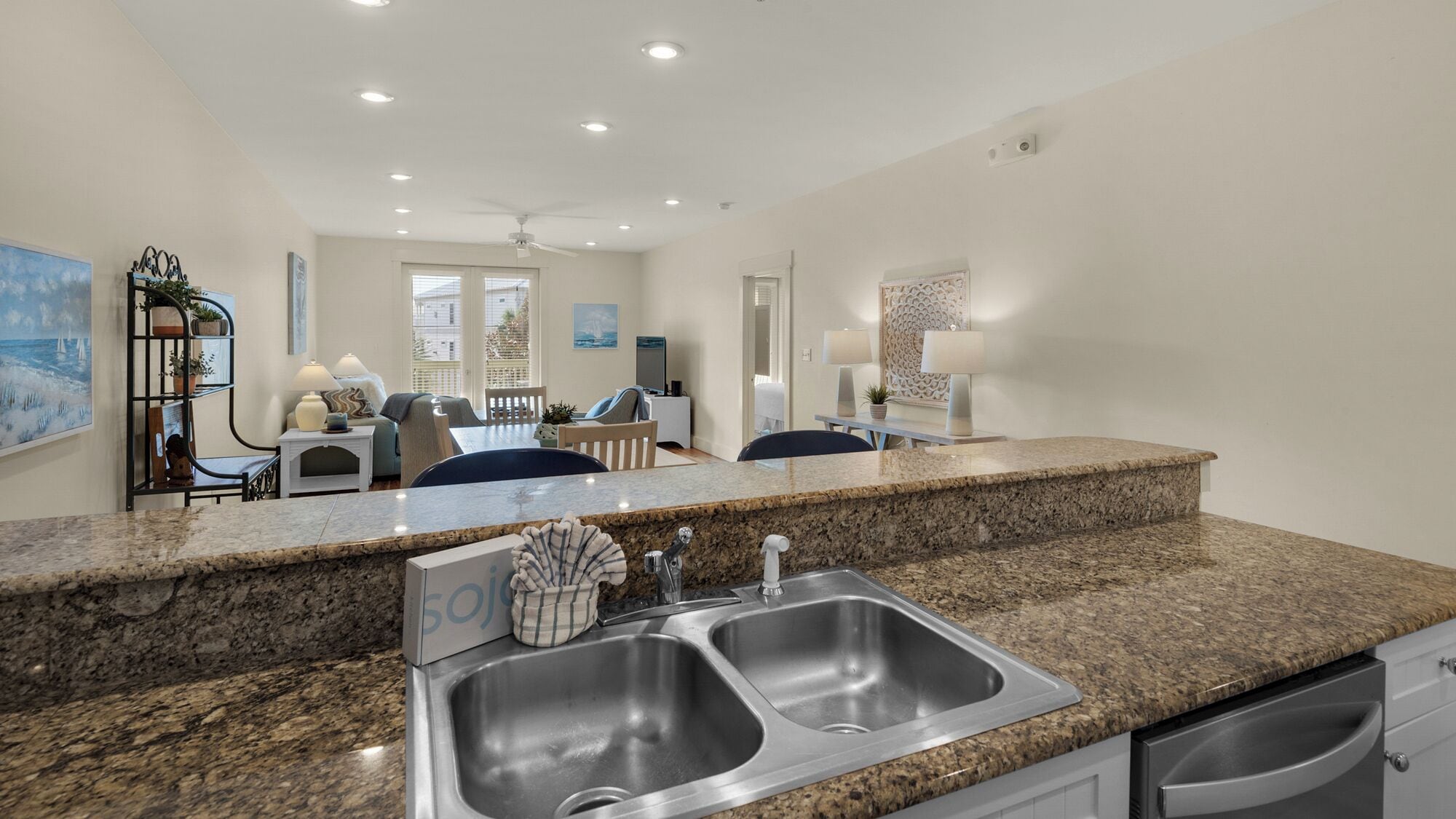 A modern kitchen with granite countertops, stainless steel sinks, and a dining area with a table and chairs.