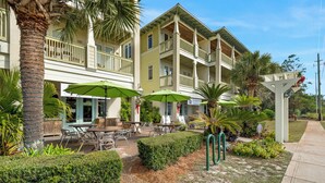 A hotel with outdoor seating, palm trees, and a covered patio area. - Grand Isle (Santa Rosa Beach)