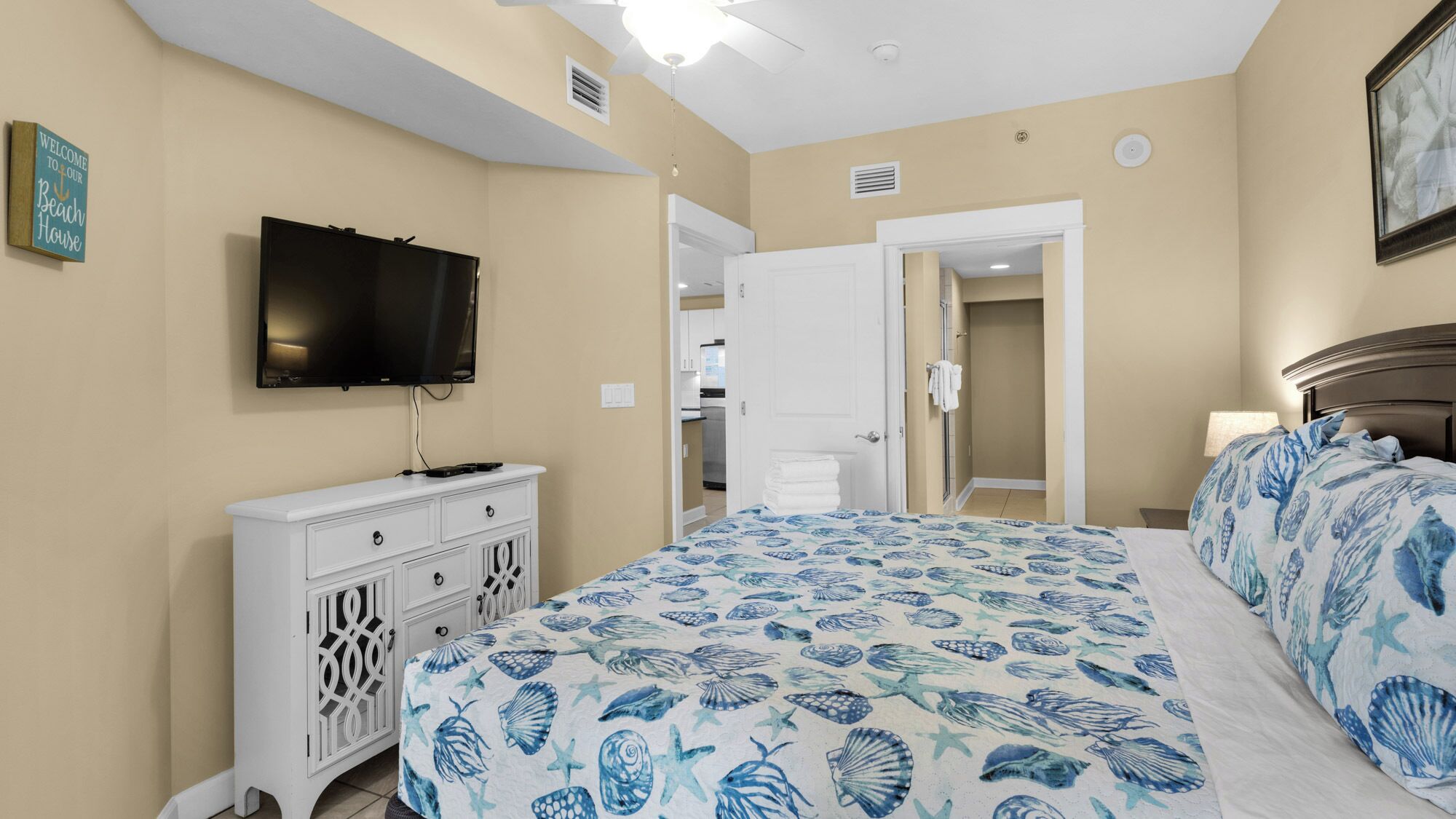 A bedroom with a bed, a TV, a dresser, and a door leading to a bathroom.