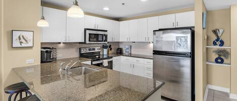 A modern kitchen with granite countertops, stainless steel appliances, and white cabinetry.