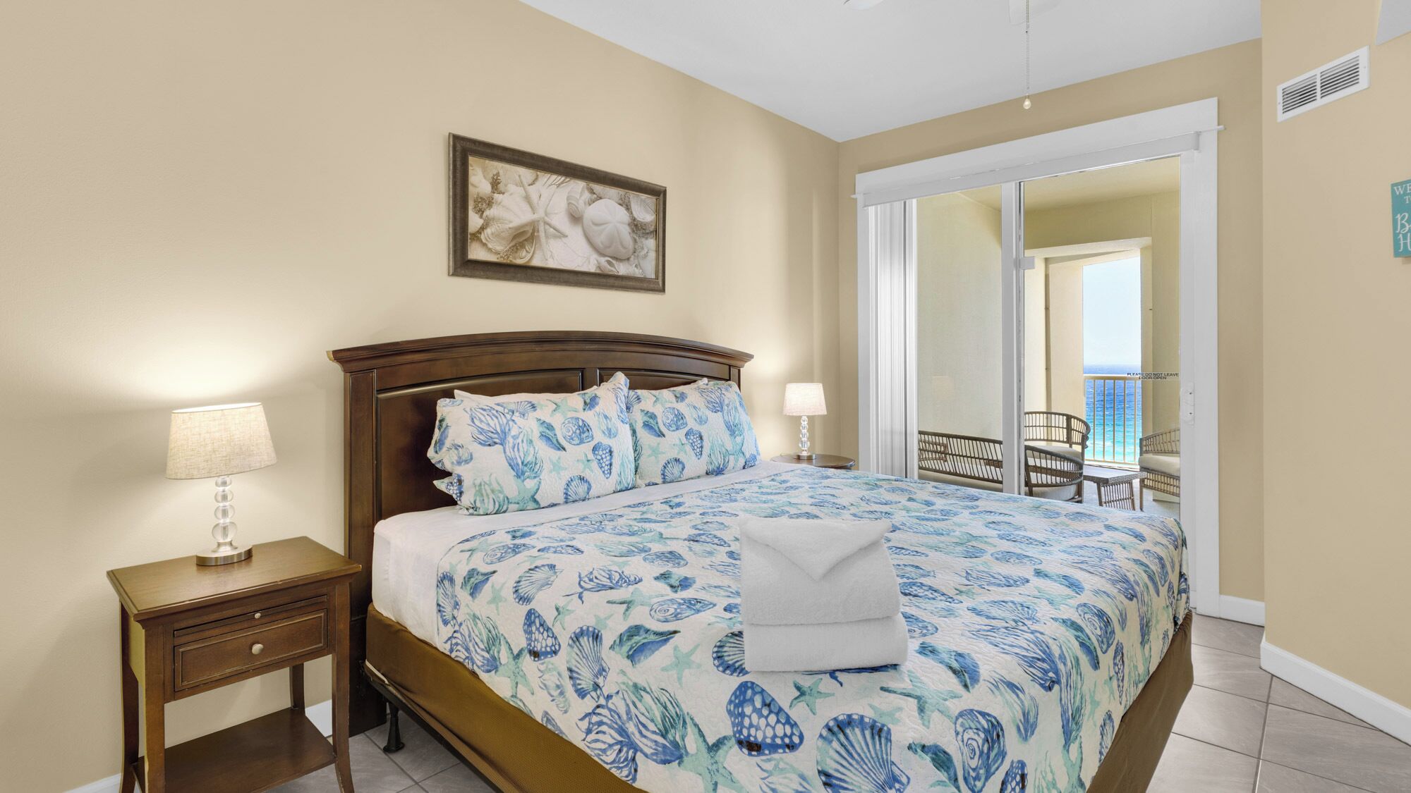 A bedroom with a bed, nightstands, a painting, and a view of the balcony.