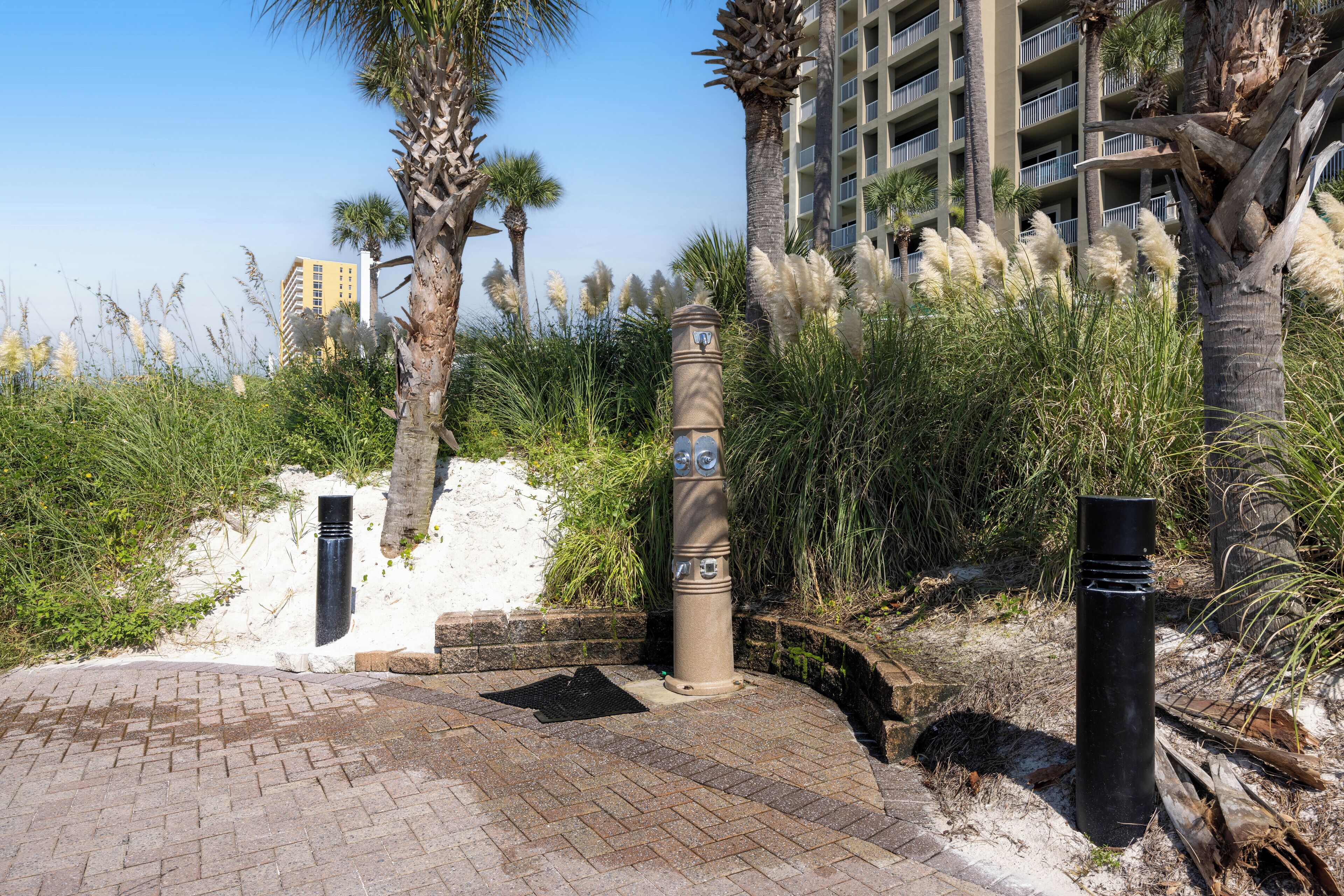 A paved pathway with a bollard, palm trees, and a building in the background.