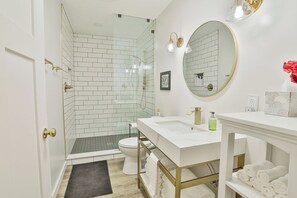 A modern bathroom with a glass shower enclosure, a white sink with gold fixtures, and a large mirror.