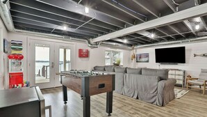 Un salon moderne avec une table de baby-foot, un canapé gris et un téléviseur à écran plat fixé au mur.