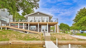 Une maison moderne dotée d’un balcon donnant sur une étendue d’eau, un quai et une zone herbeuse avec des arbres.
