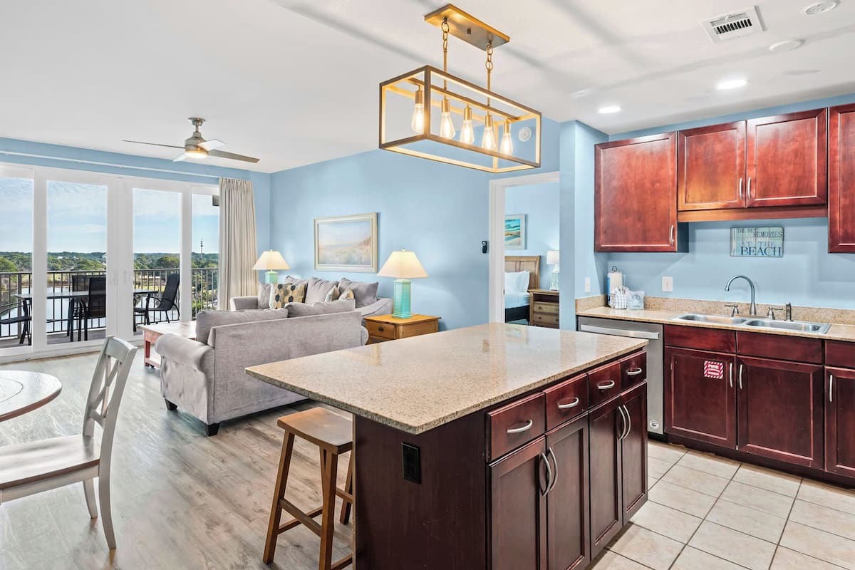 A modern kitchen with wooden cabinets, a central island, and a dining area with a round table and chairs.