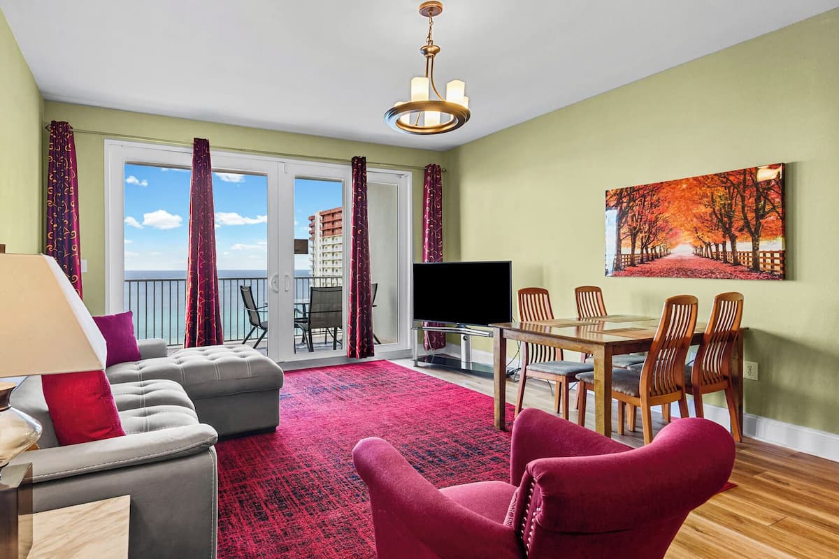 A living room with a sofa, a red armchair, a TV, and a dining area with chairs and a table.