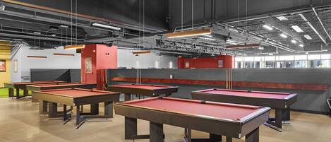 A billiards hall with multiple red pool tables, a red machine, and a grey wall with windows.