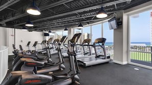 A gym with treadmills and elliptical machines, large windows, and a view of the ocean. - Laketown Wharf (Panama City Beach)