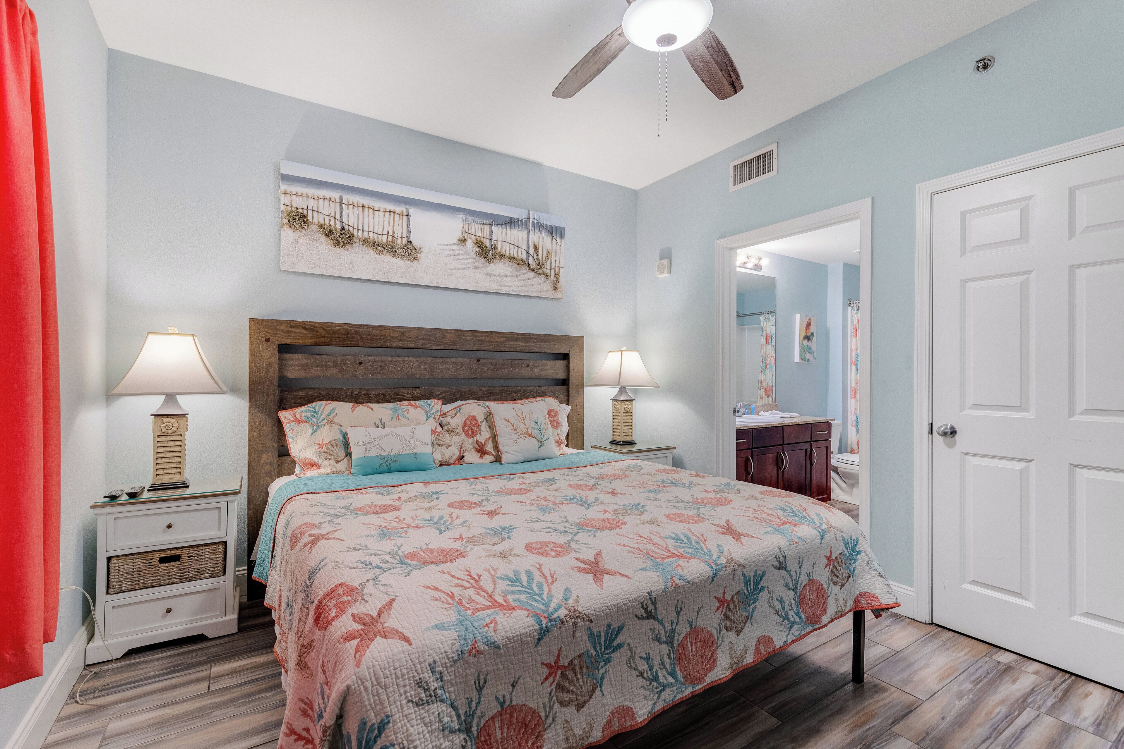 A bedroom with a bed, nightstands, a ceiling fan, a painting, and a door.