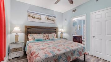 A bedroom with a bed, nightstands, a ceiling fan, a painting, and a door.