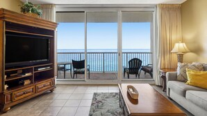 Una sala de estar con un televisor de pantalla plana grande, un mueble de madera para entretenimiento, un sofá, una mesa de centro y un balcón con vista al océano.