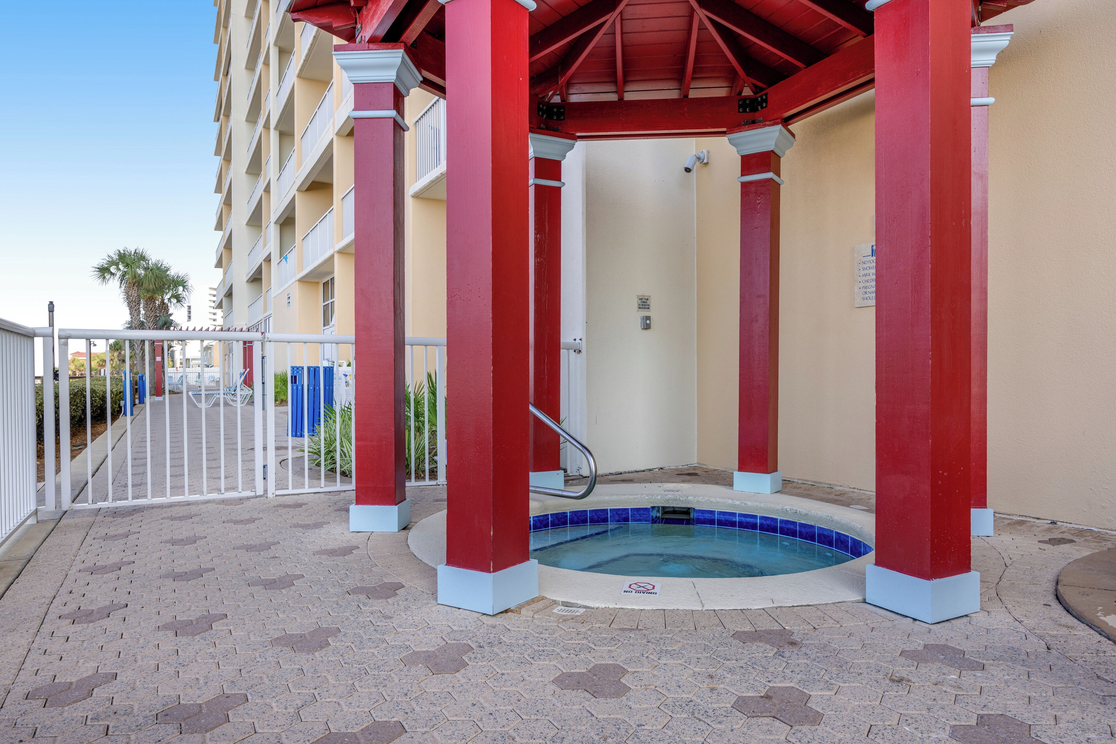A covered outdoor pool area with red pillars, a white gate, and a beige building in the background.