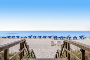 Una playa con pasarelas de madera que conducen a sillas y sombrillas azules.