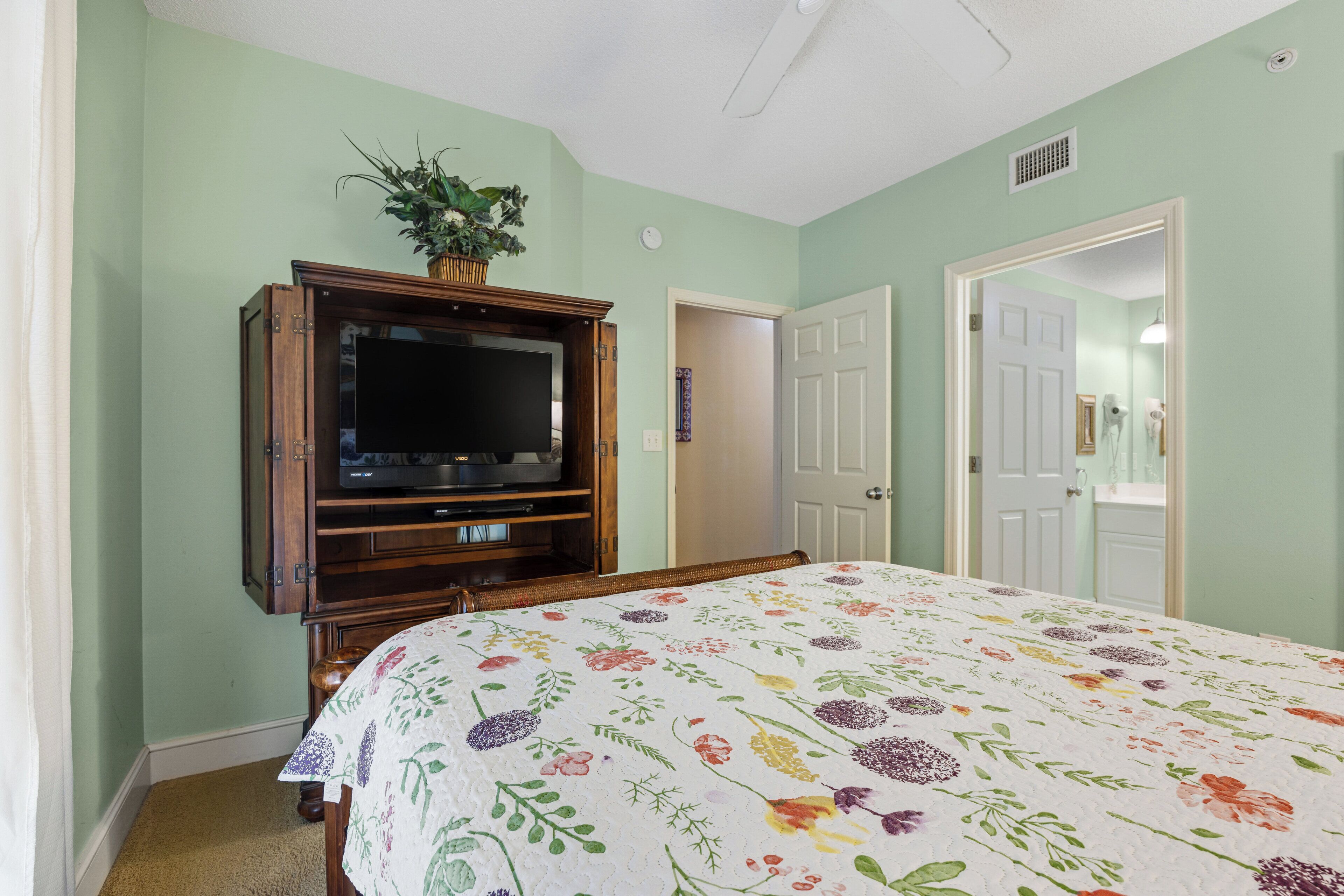 A bedroom with a bed, a television on a wooden stand, and a door leading to another room.