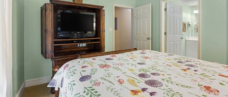 A bedroom with a bed, a television on a wooden stand, and a door leading to another room.