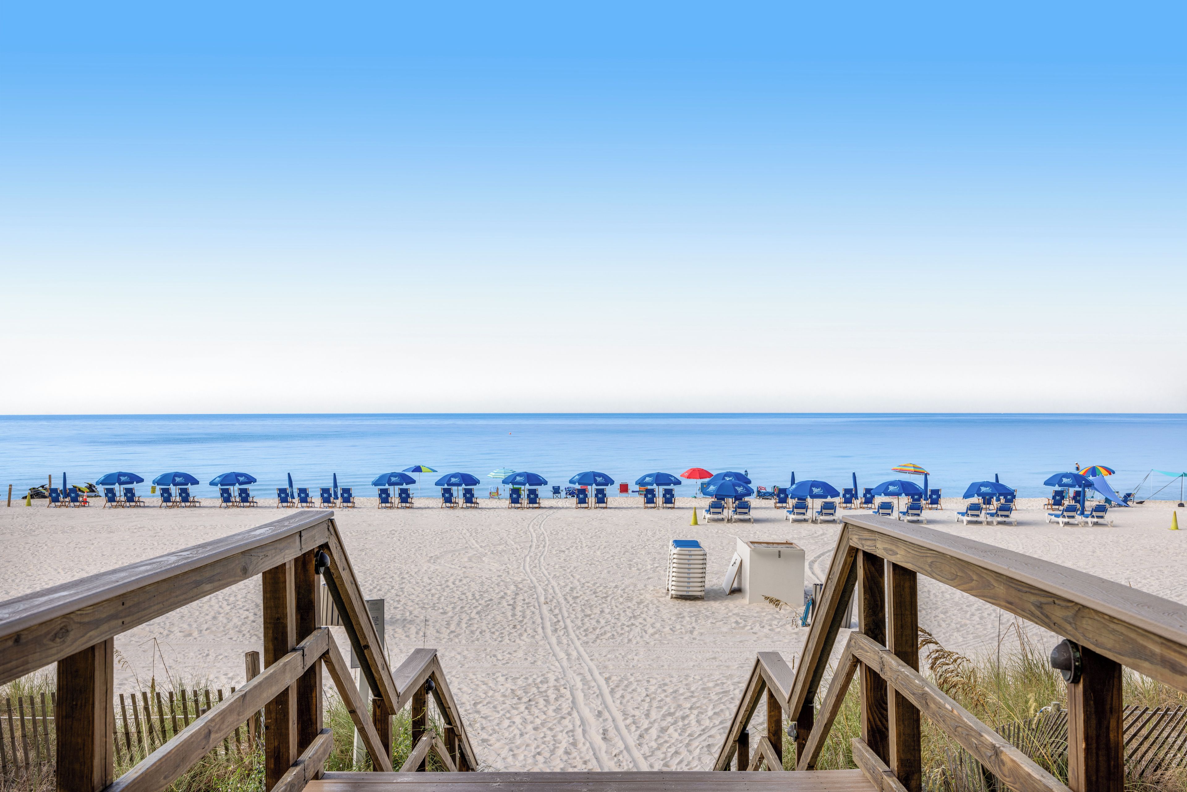 A beach with wooden walkways leading to blue beach chairs and umbrellas.