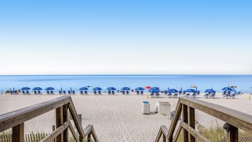 A beach with wooden walkways leading to blue beach chairs and umbrellas.