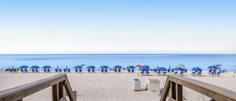 A beach with wooden walkways leading to blue beach chairs and umbrellas.