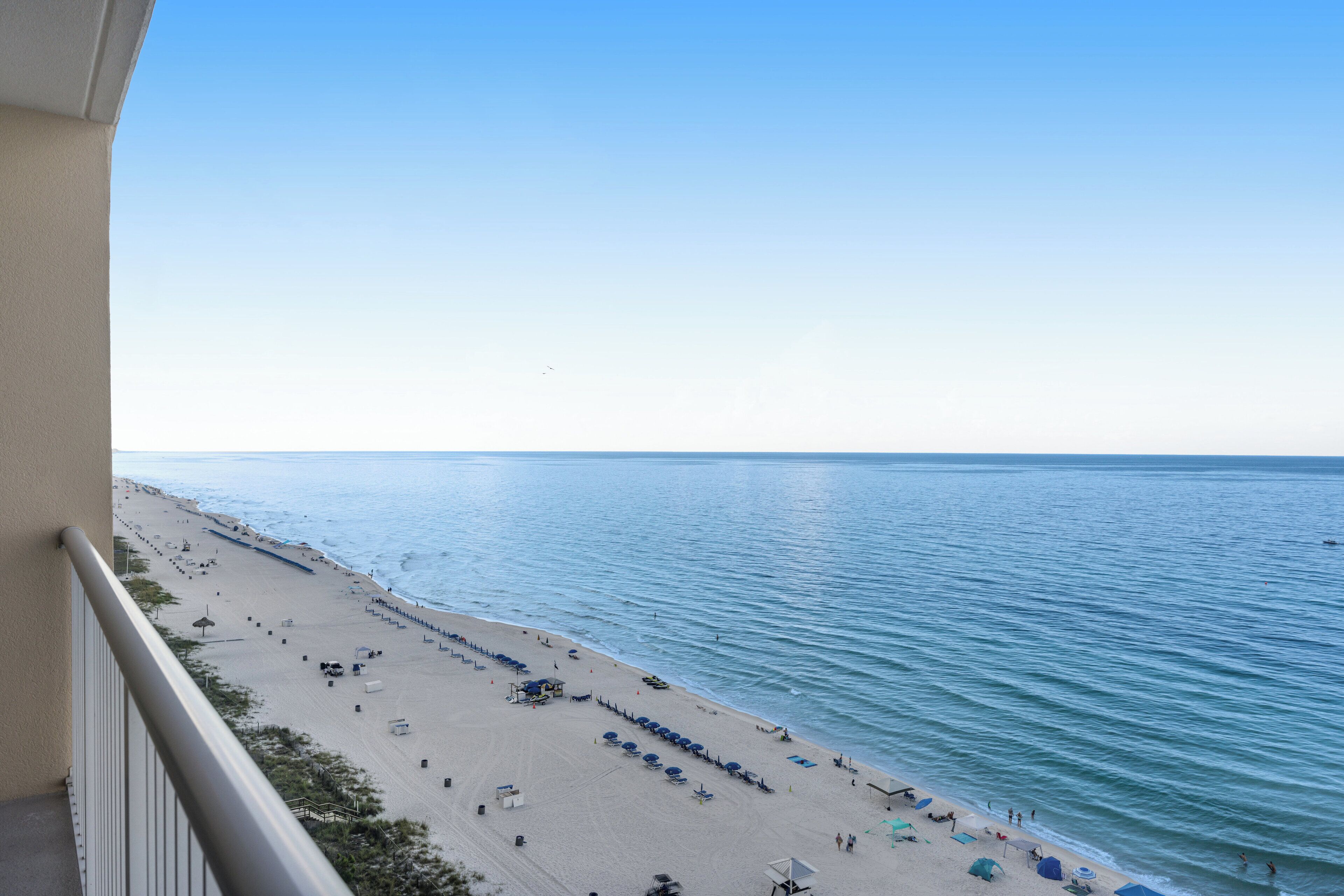Vista di una spiaggia dal balcone, con file di ombrelloni e lettini.
