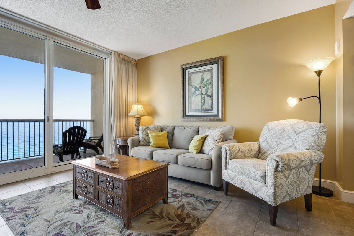 A living room with a sofa, armchair, coffee table, and a painting on the wall.