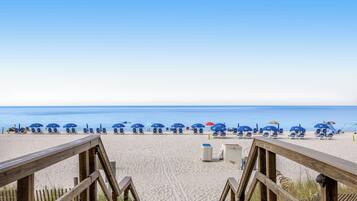 A beach with wooden walkways leading to blue beach chairs and umbrellas.