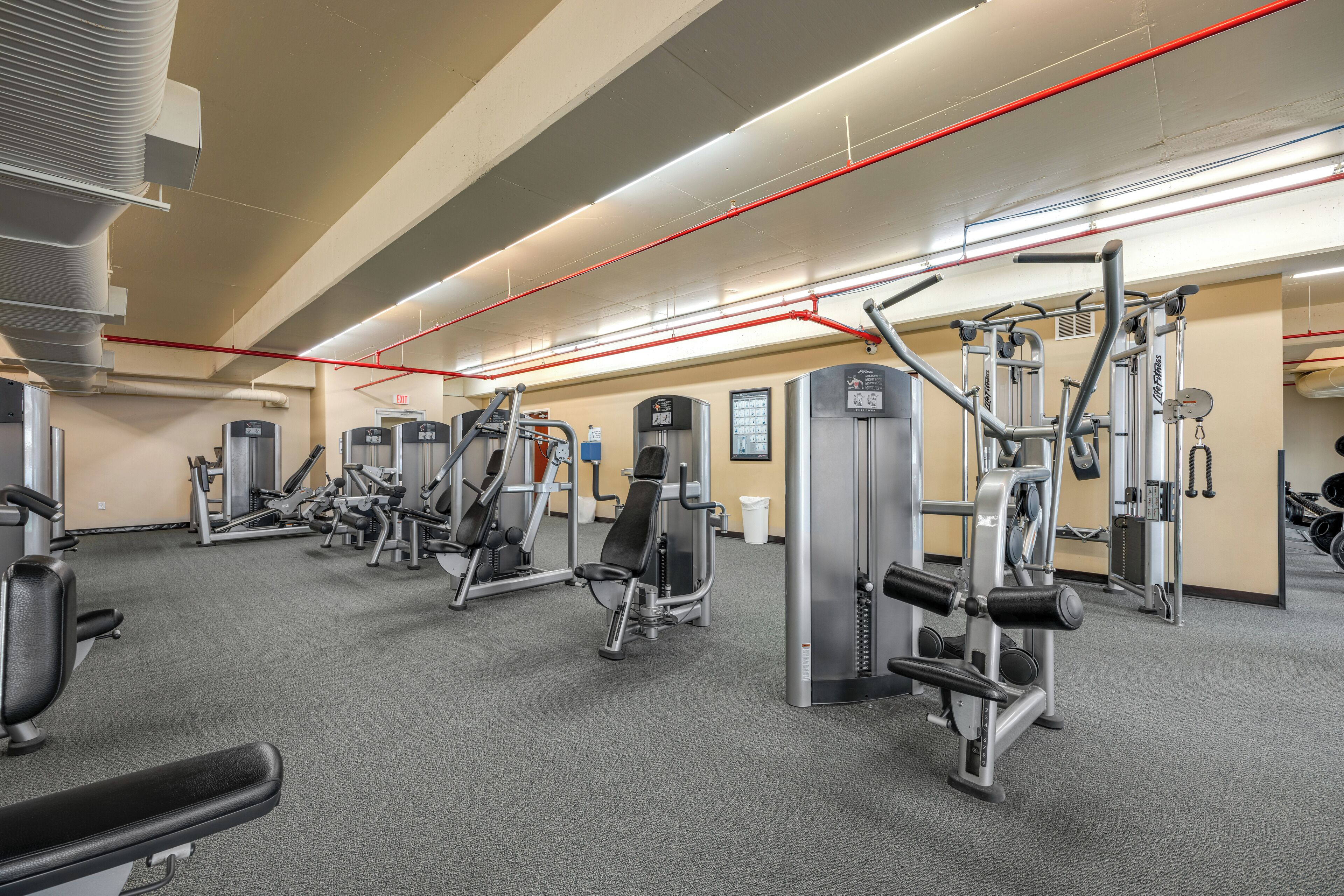 A gym with various exercise machines, a bench, and a wall-mounted mirror.