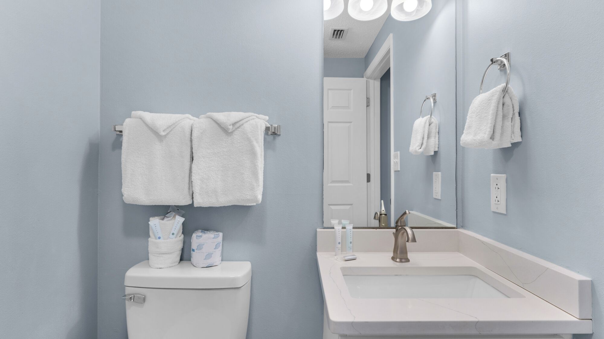 Un baño con inodoro, lavamanos y dos toallas colgadas en la pared.