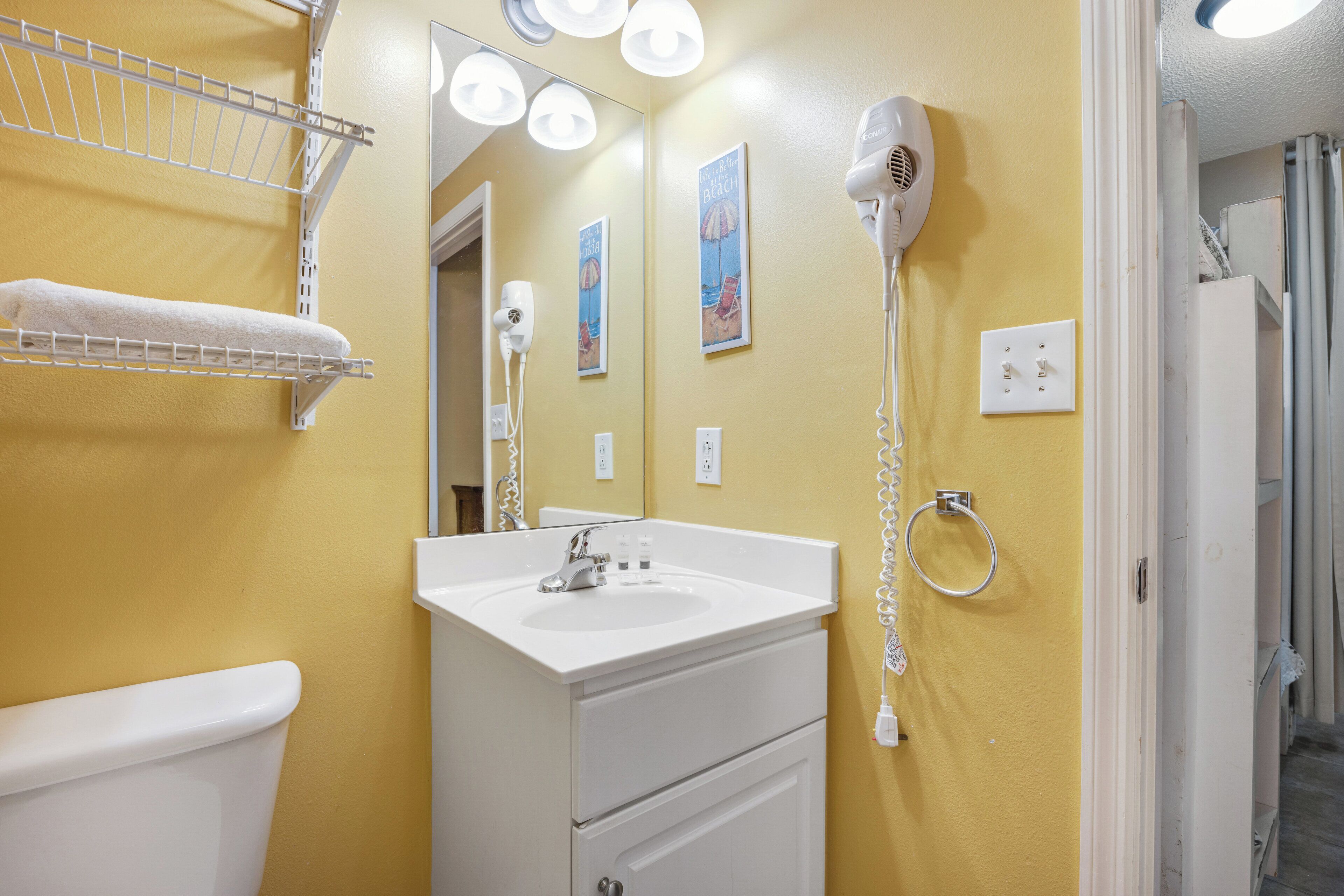 A bathroom with a yellow wall, white sink, and a hairdryer mounted on the wall.