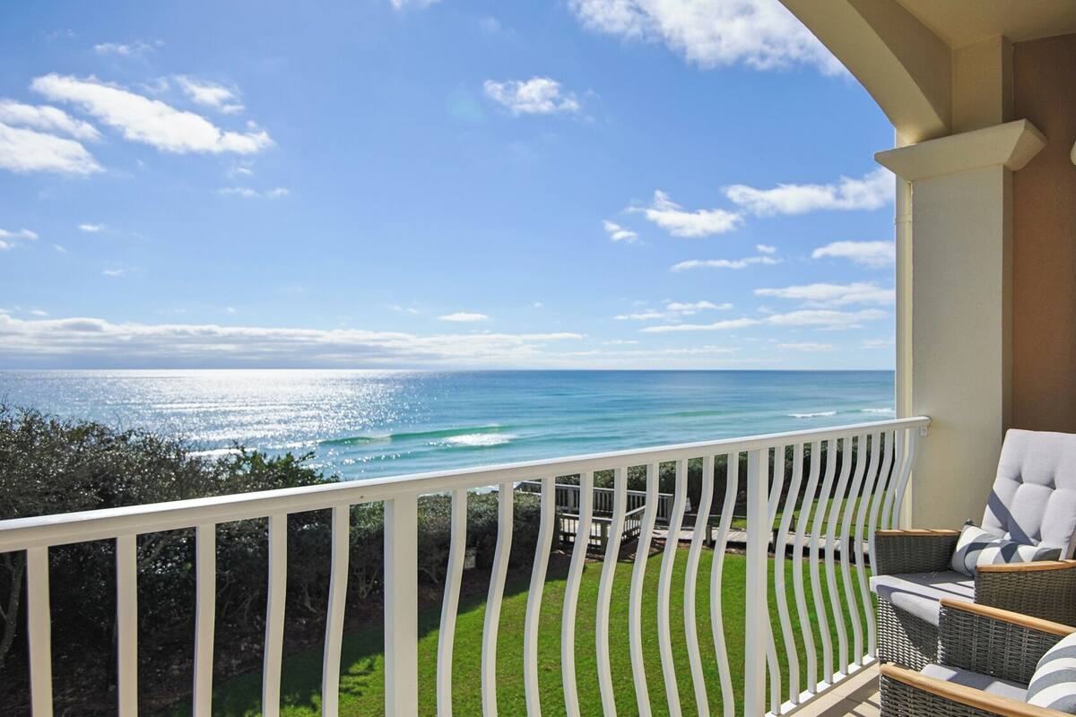 A balcony with a view of the ocean, wicker furniture, and a white railing.