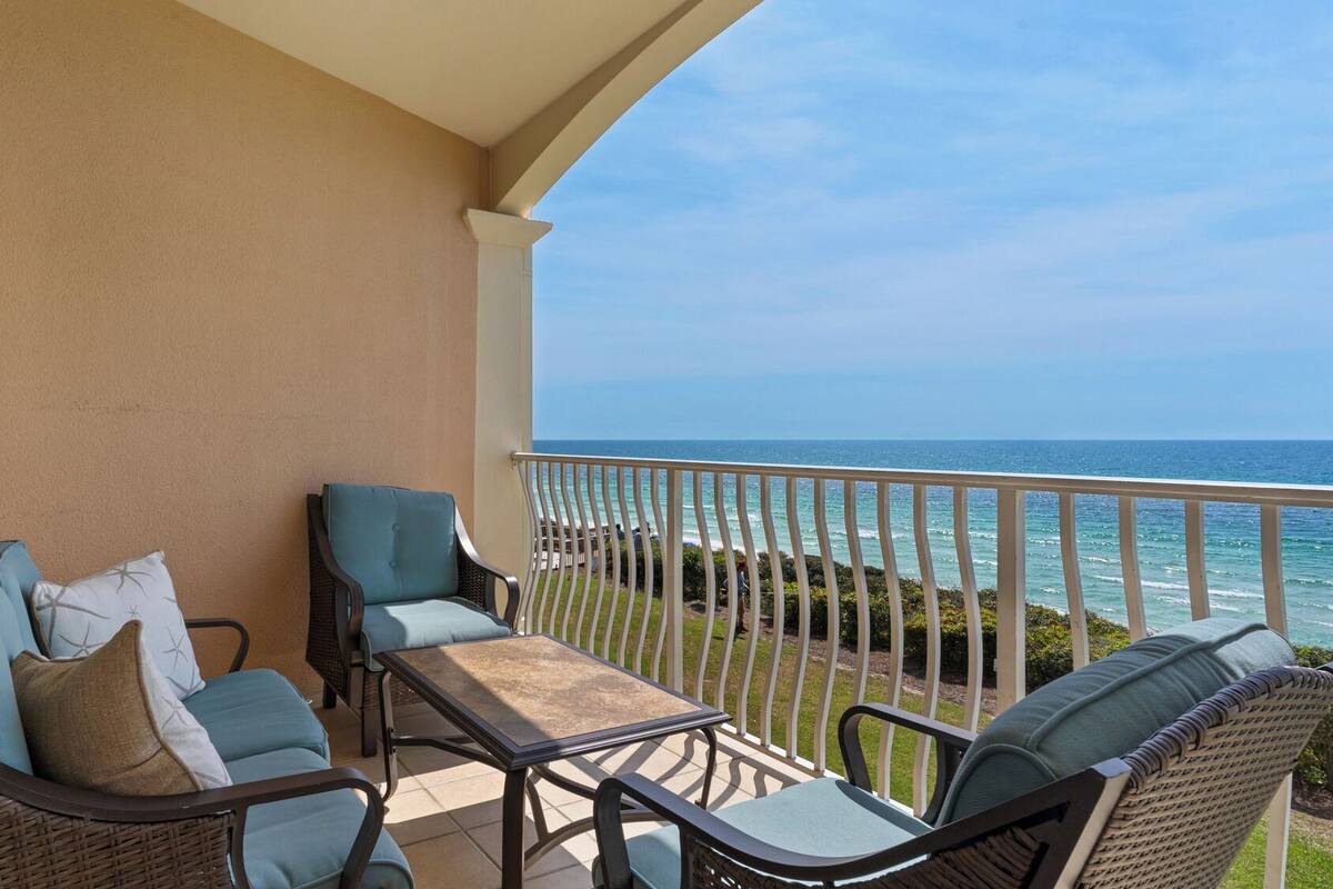A balcony with wicker furniture, a view of the ocean, and a clear sky.