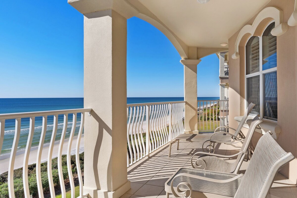 A balcony with a view of the ocean, white railings, and outdoor furniture.