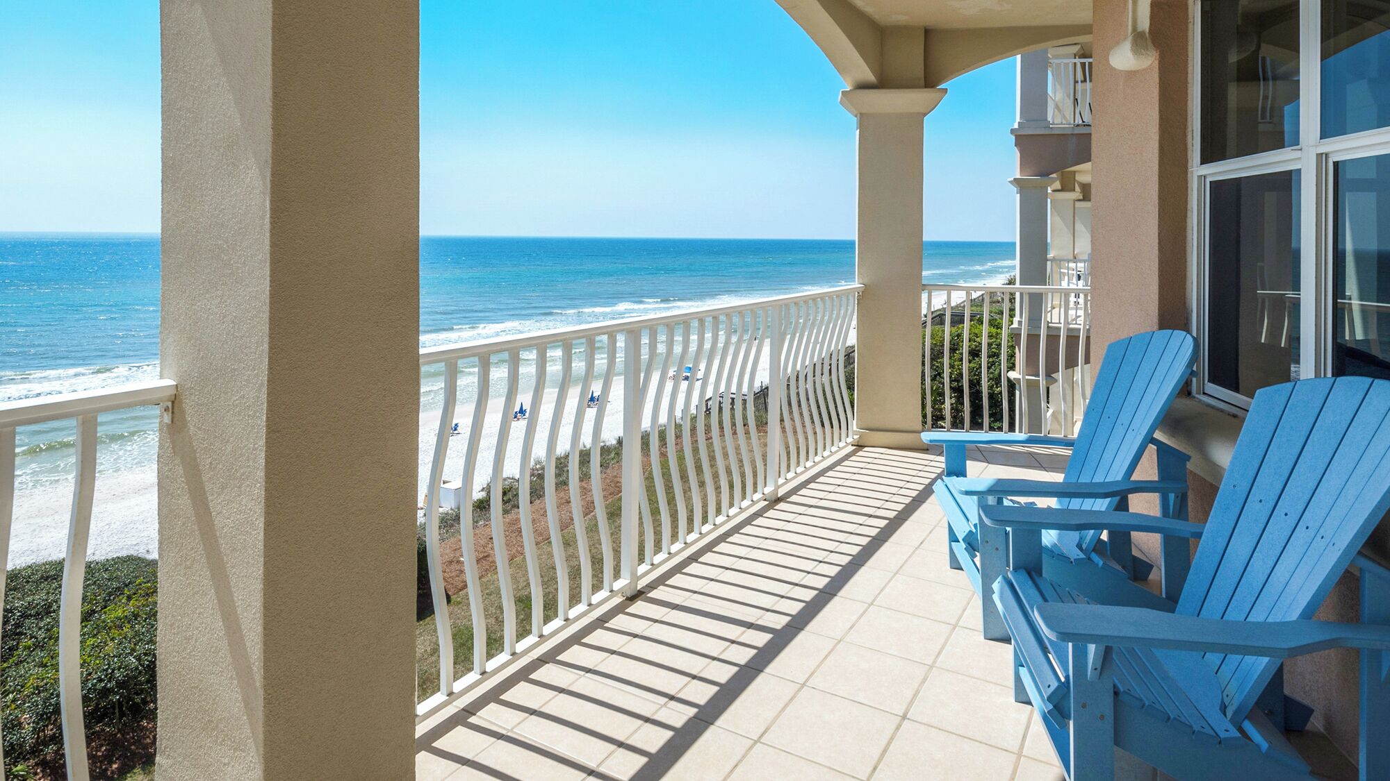 A balcony with a view of the ocean, blue chairs, and a white railing.