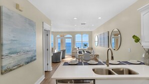 A spacious kitchen with a large island, a dining area with a view, and a living space with a large painting. - Monterey Condos (Panama City Beach)