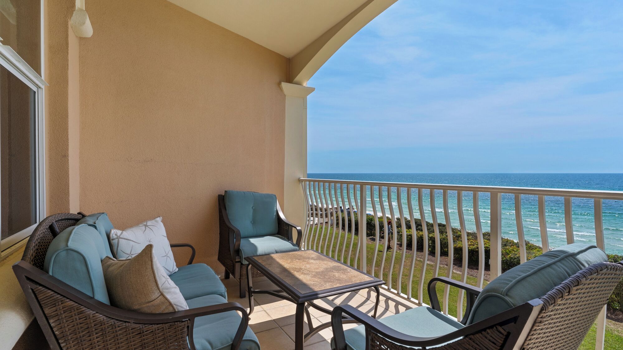 A balcony with wicker furniture, a view of the ocean, and a clear sky.