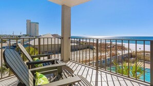 A balcony with a view of the beach and ocean, featuring lounge chairs and a pool. - Moondrifter Condominiums (Panama City Beach)