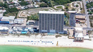 Eine Vogelperspektive eines Hotels mit großem Parkplatz, einem Schwimmbad und einem Strandbereich mit Sonnenschirmen.