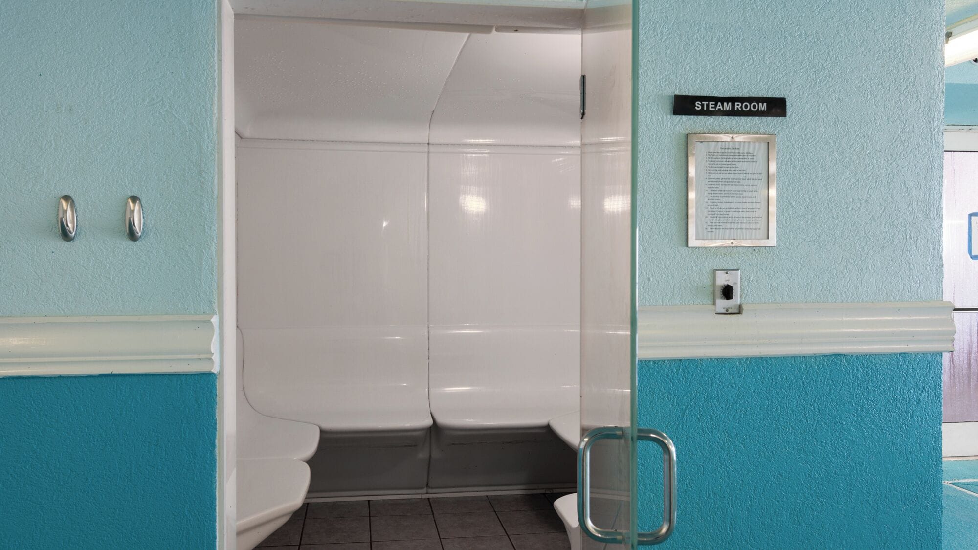 A steam room with a sign above the door, a handrail, and a wall-mounted information board.