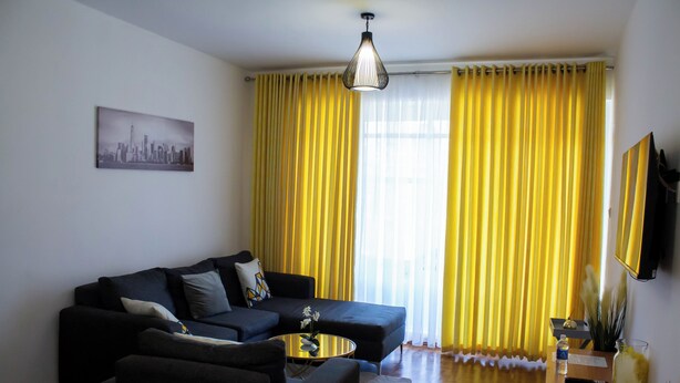 A living room with a sectional sofa, a coffee table, and a painting on the wall. - Apartment Sleeps 4, 2 Baths, Free Parking (Harare)