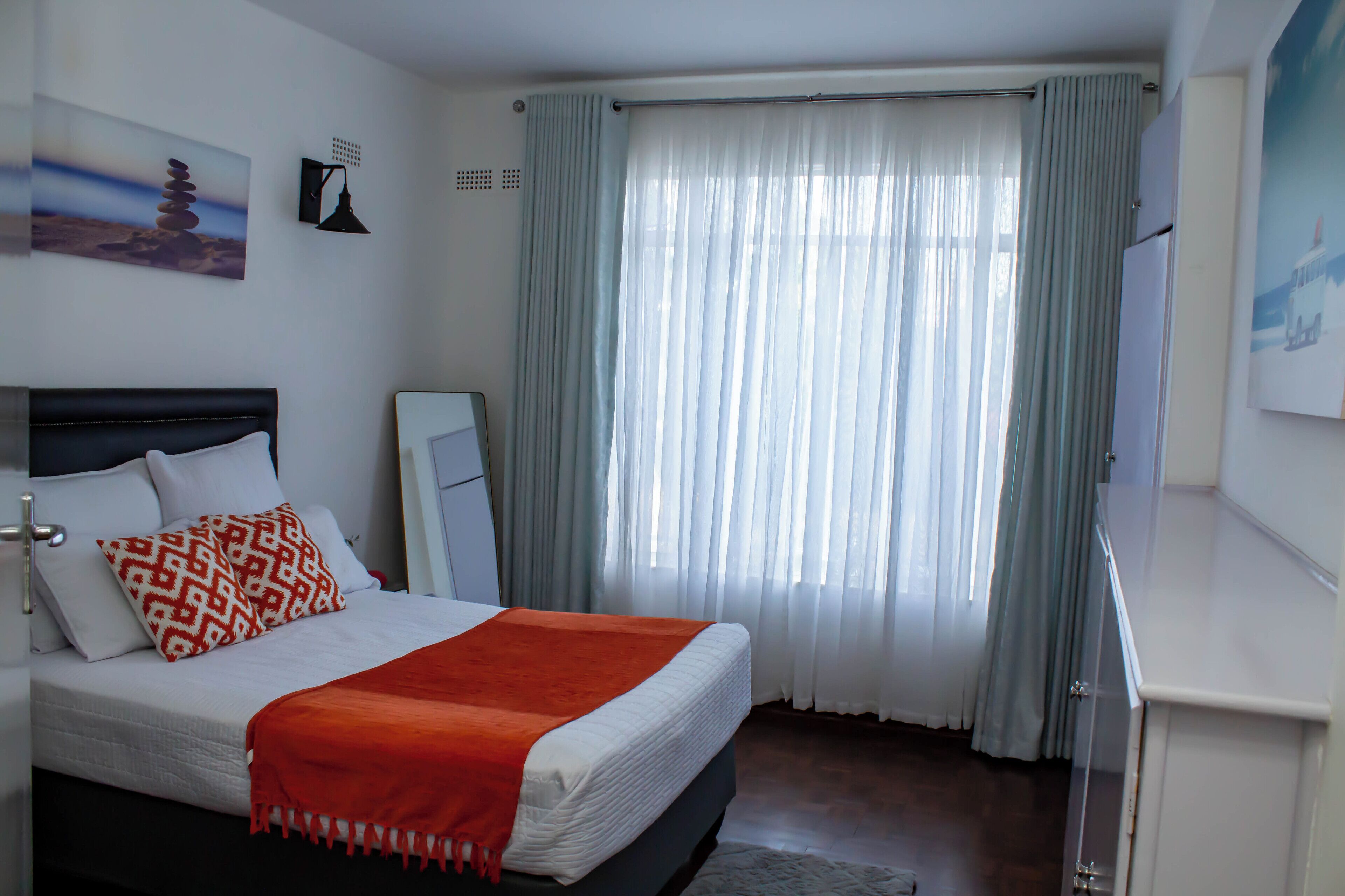 Ein Schlafzimmer mit einem Bett, einem Schreibtisch, einem Sessel, einem Fenster mit Vorhängen und einem Bild an der Wand.
