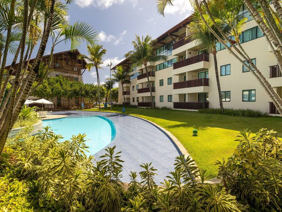 Un resort con piscina, abundante vegetación y edificios de varios pisos con balcones.