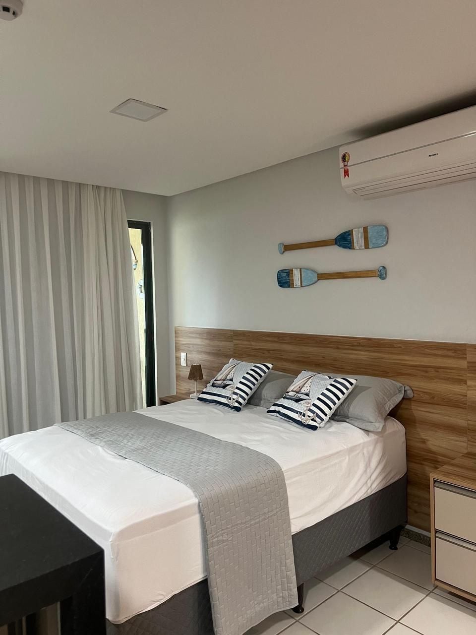 Quarto moderno com cama, mesas de cabeceira e ar condicionado fixado na parede.