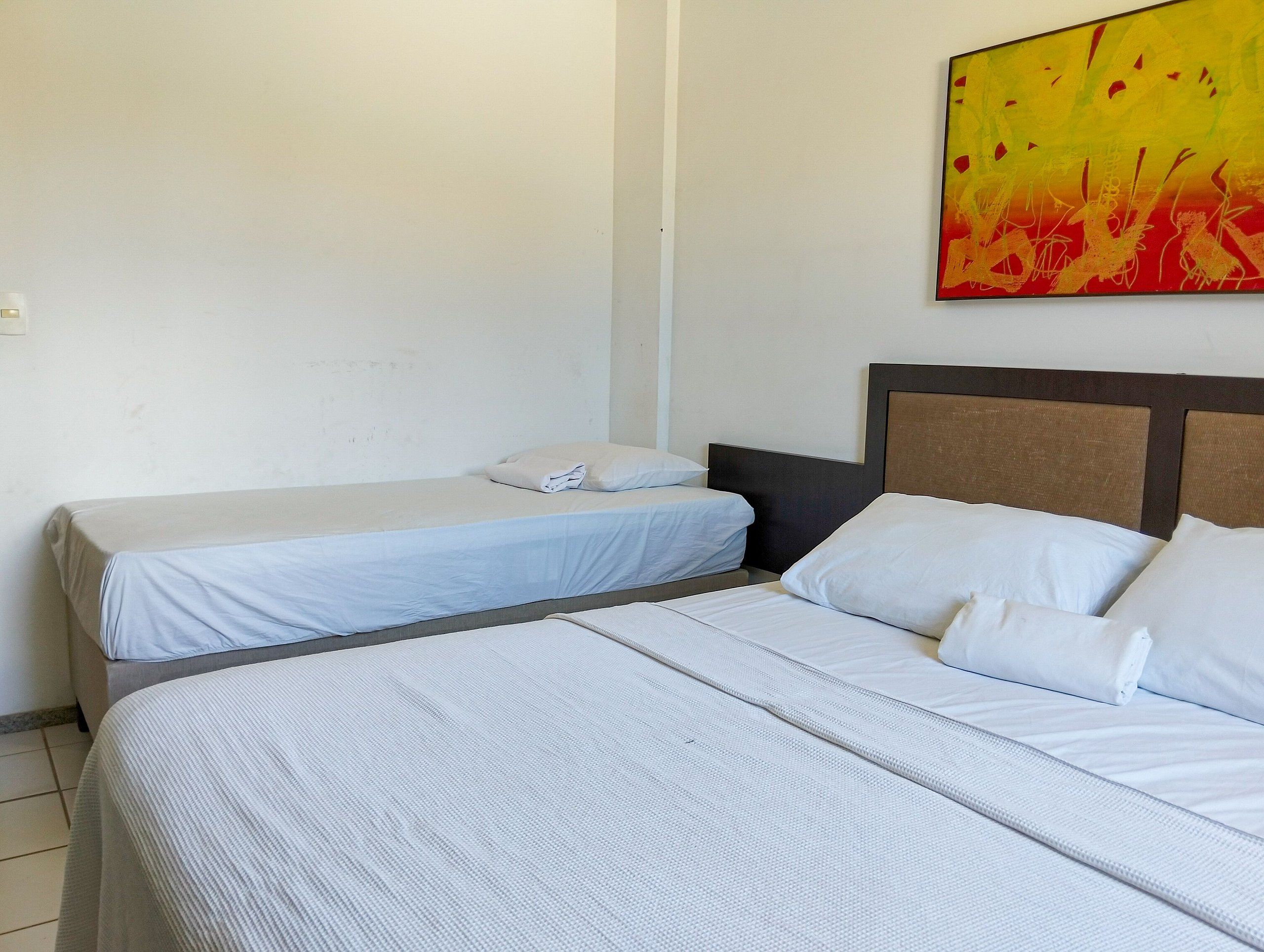 A hotel room with two single beds, a large bed, and a painting on the wall.