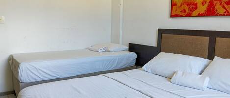 A hotel room with two single beds, a large bed, and a painting on the wall.