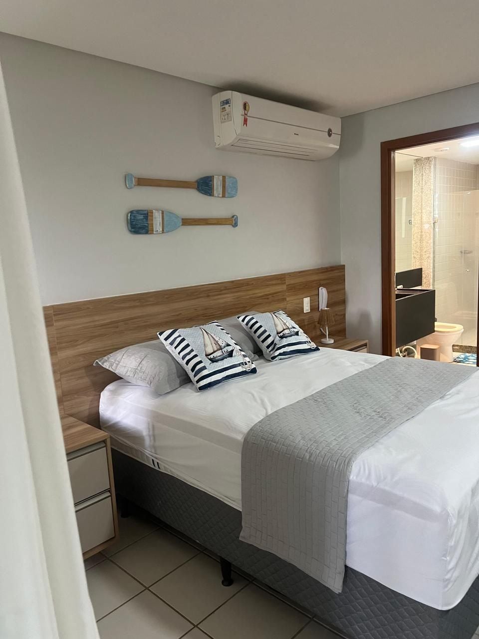A neatly made bed with striped pillows, a wooden headboard, and an air conditioning unit above.
