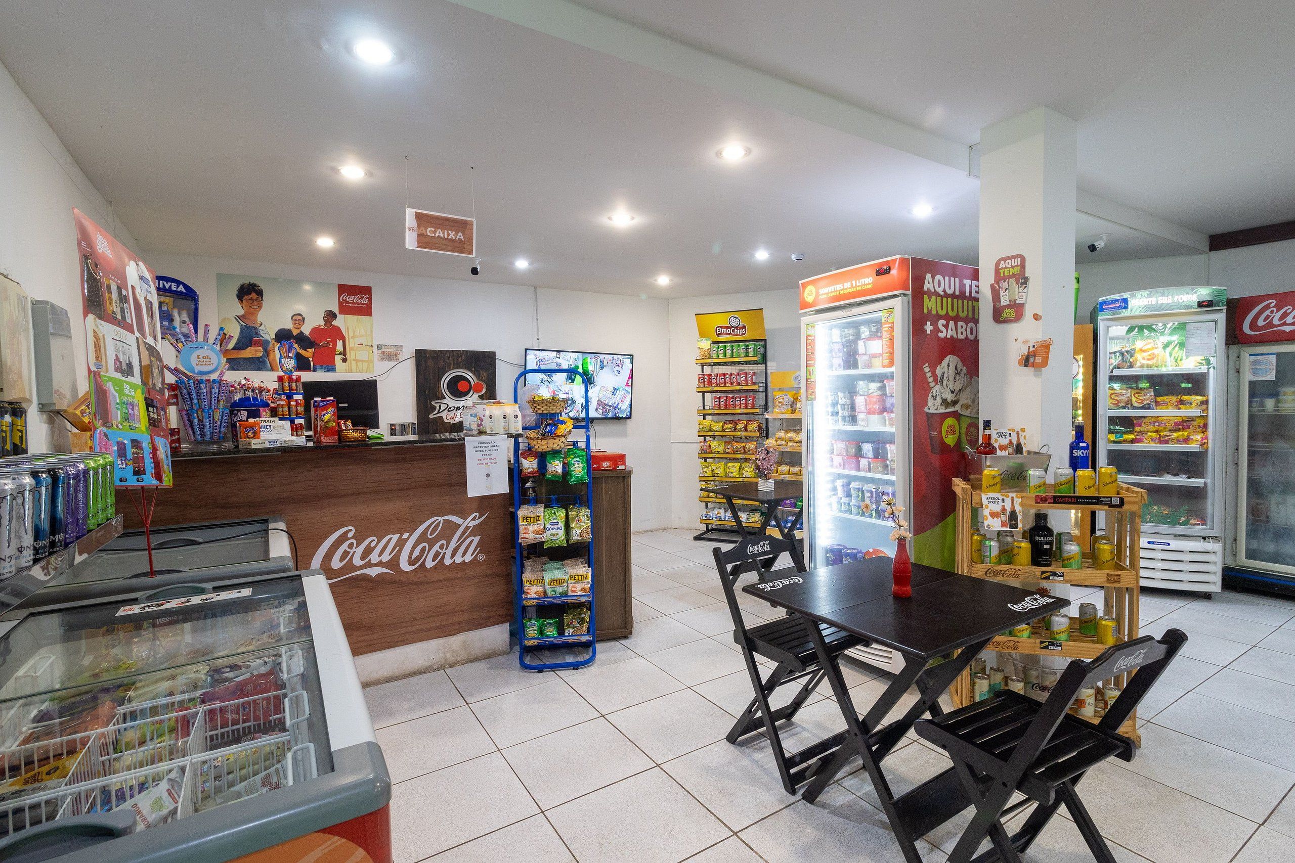 Uma loja de conveniência limpa e bem iluminada, com um refrigerador de Coca-Cola, prateleiras cheias de lanches e uma máquina de venda automática de Coca-Cola.